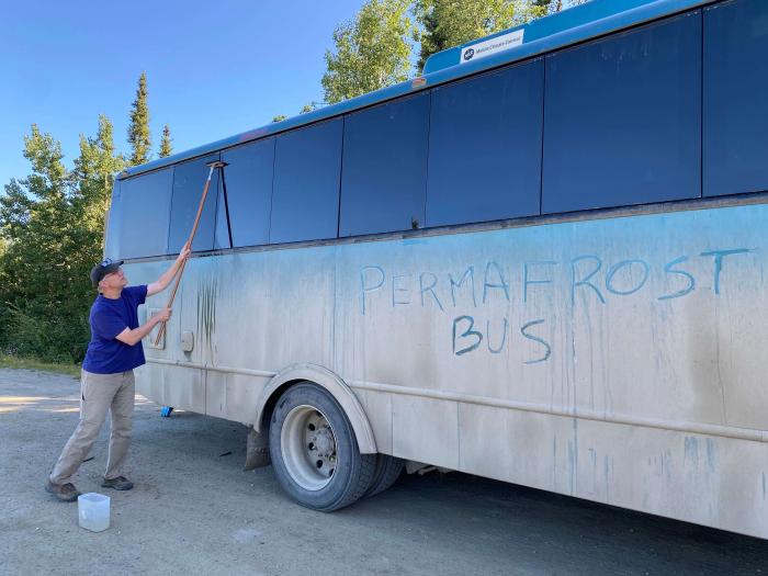 Figure 8. Transportation for the second half of the Symposium was provided by Fairbanks-based Northern Alaska Tour Company. NATC guide, John Peirce, washes the windows of the 24-passenger coach that provided facilities for a rolling workshop in the Prudhoe Bay Oilfield and along the Dalton Highway. Battelle ARO managed logistics for the Symposium. Photo courtesy of Jana Peirce.